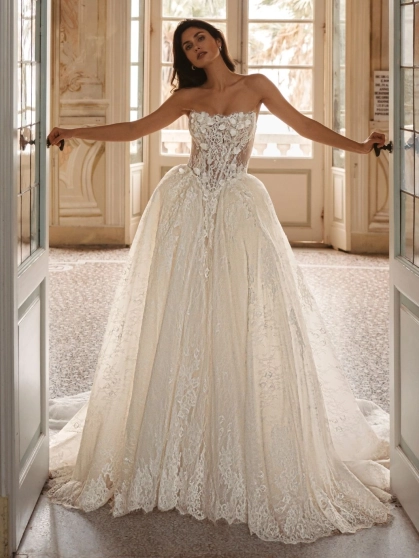 Enzoani Waylen luxury wedding dress with a strapless sweetheart neckline, intricately embroidered floral lace corset bodice, voluminous ball gown skirt, couture detailing, and dramatic cathedral train. Designer bridal gown by Enzoani combining modern roman