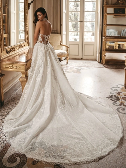 Enzoani Wednesday luxury wedding dress with a fitted mermaid silhouette, illusion halter neckline, floral lace embroidery, sculpted corset bodice, detachable overskirt, and dramatic cathedral train. Couture bridal gown by Enzoani combining modern glamour,